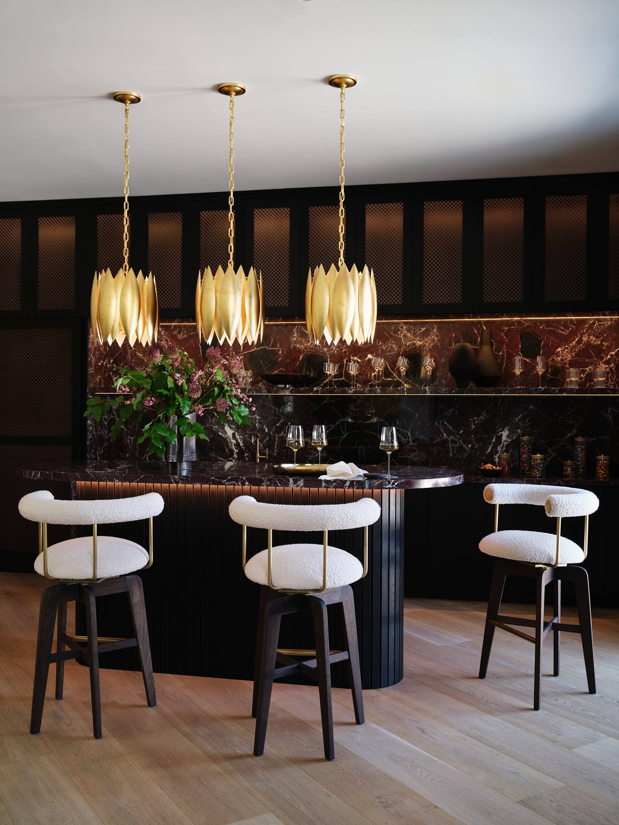 Gilded pendants over a bar with a Rosso Levanto backsplash
