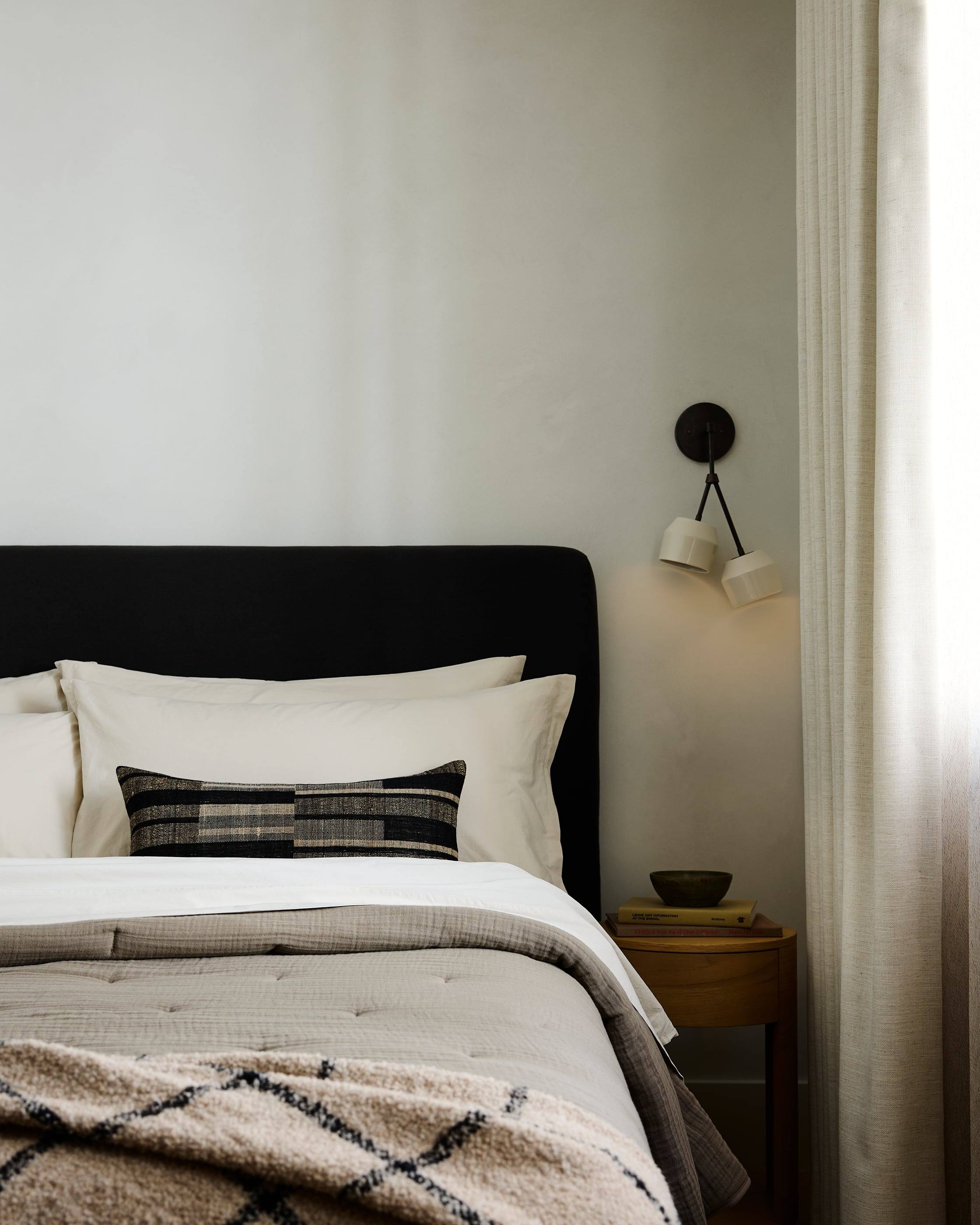 Black linen headboard with a twin ceramic sconce and sheer drapery