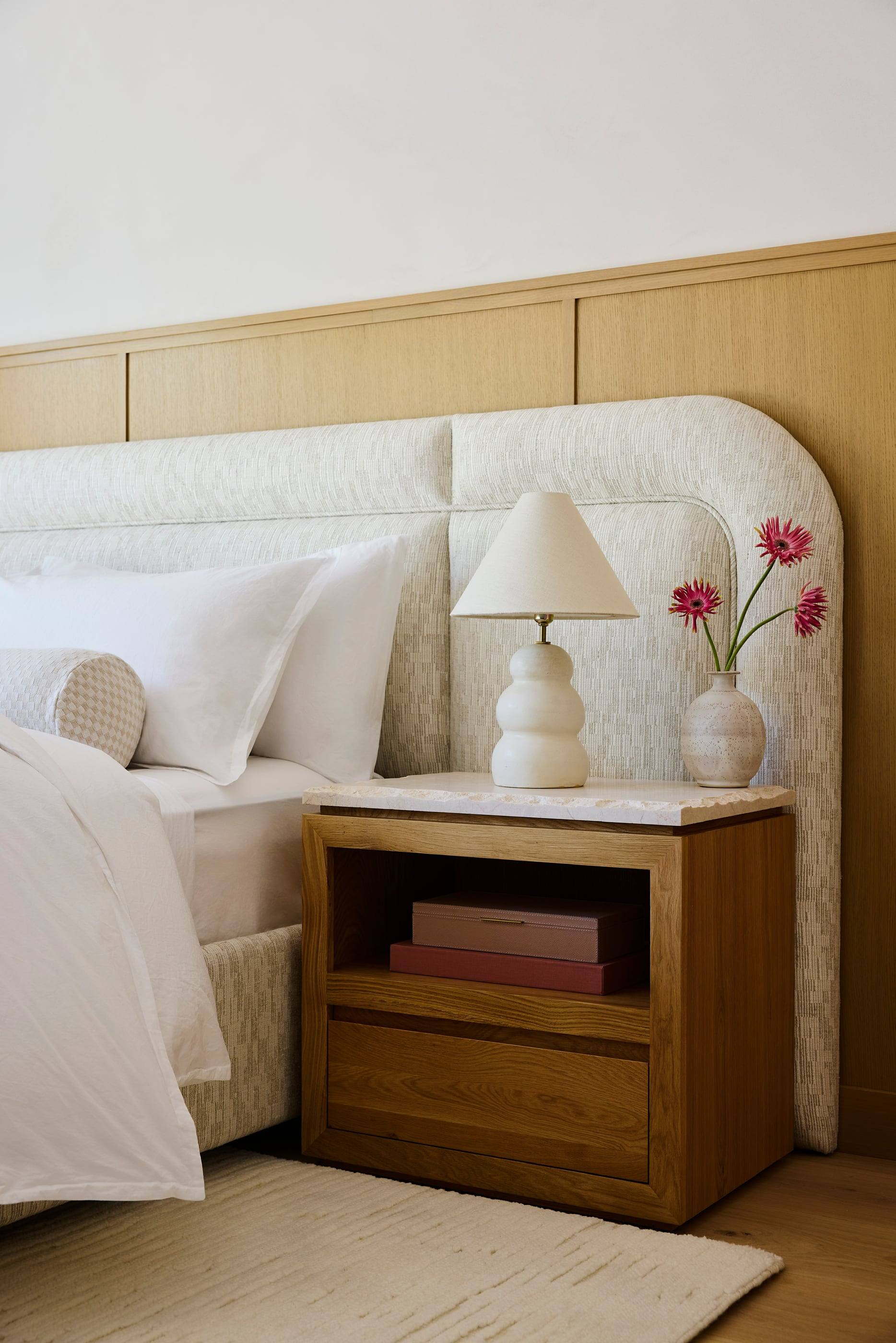 Curved upholstered headboard against oak paneling with a stone-topped nightstand