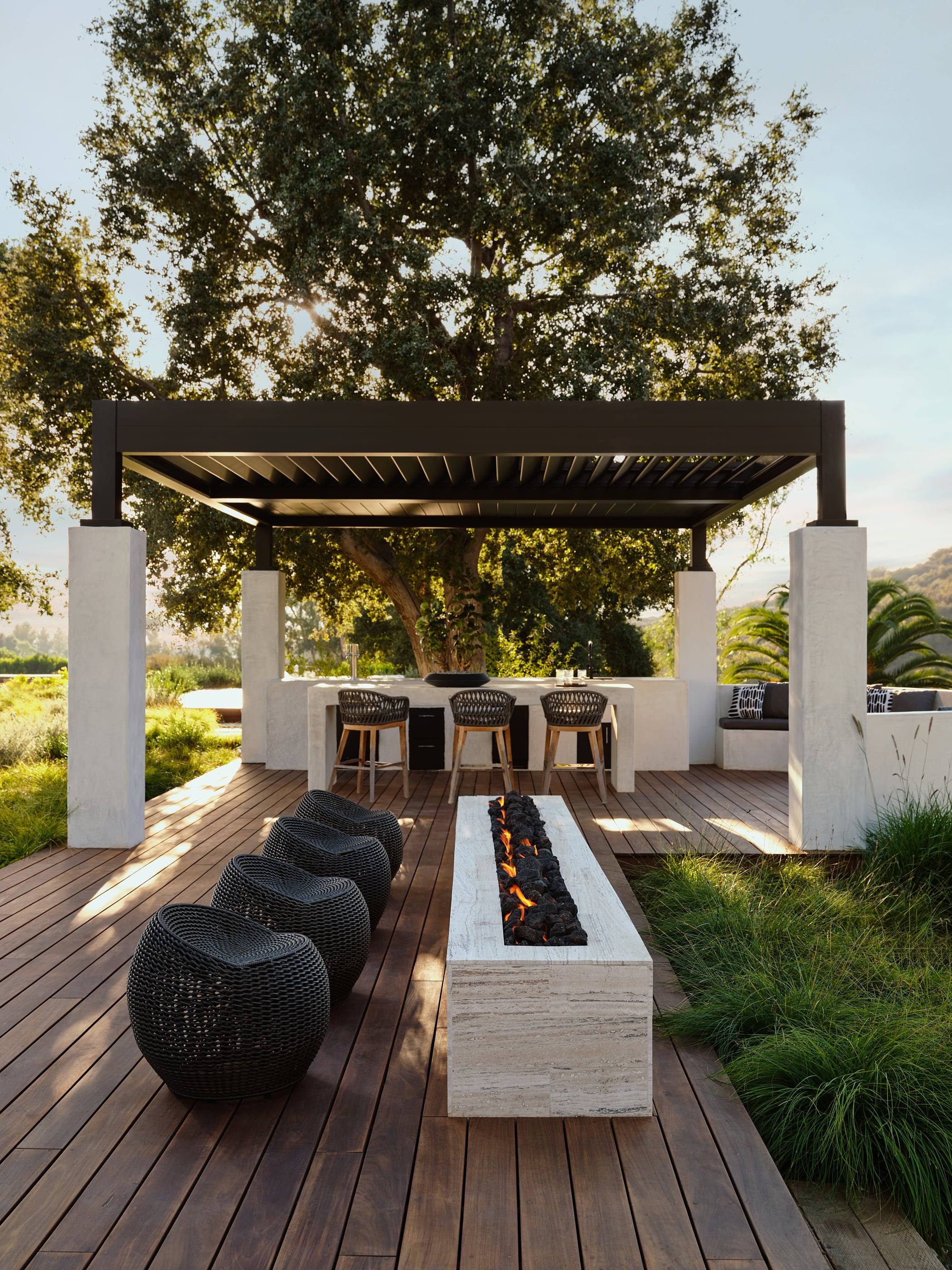 Teak terrace with a long fire table beneath a steel pergola