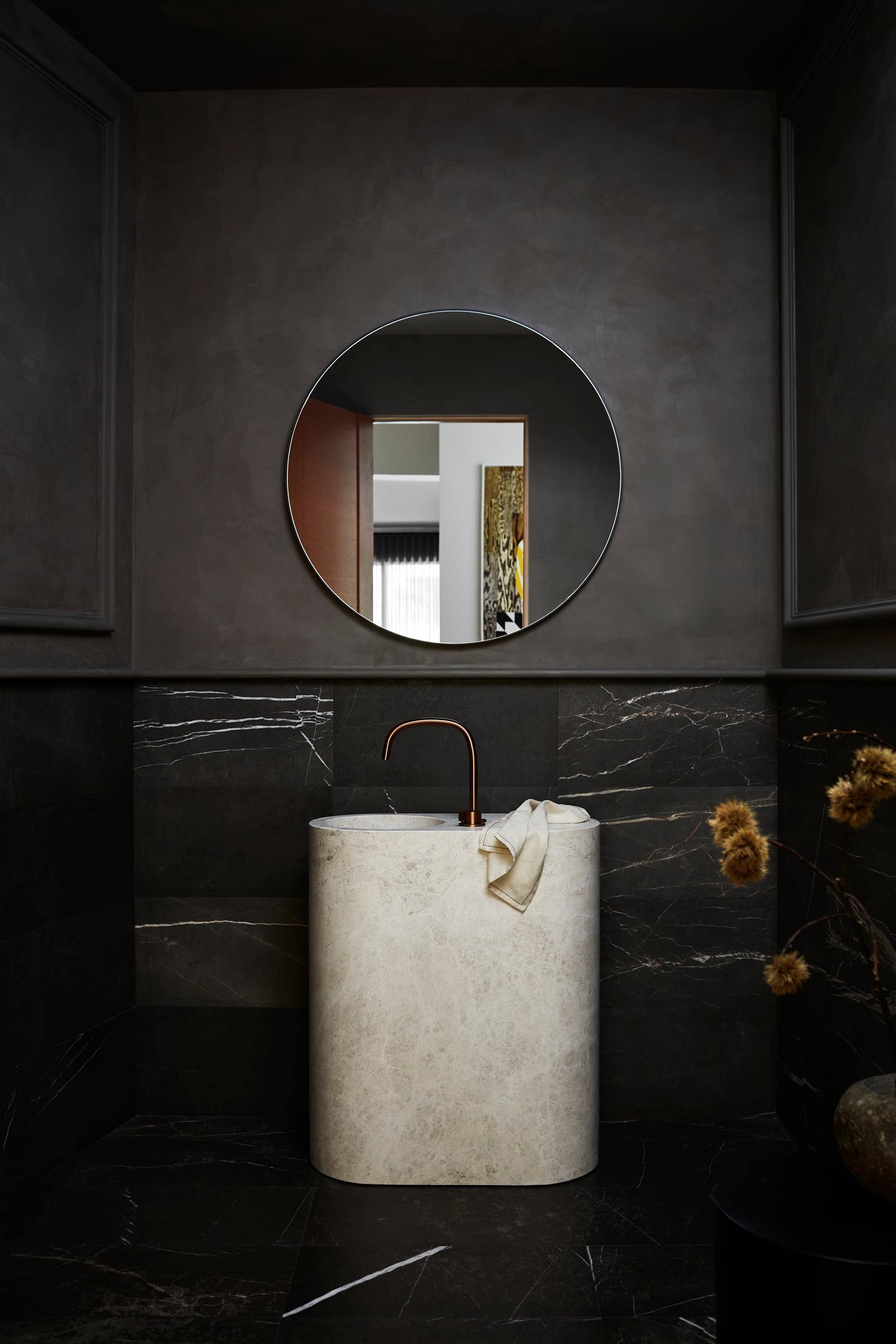 Powder room with a stone pedestal sink and a round mirror