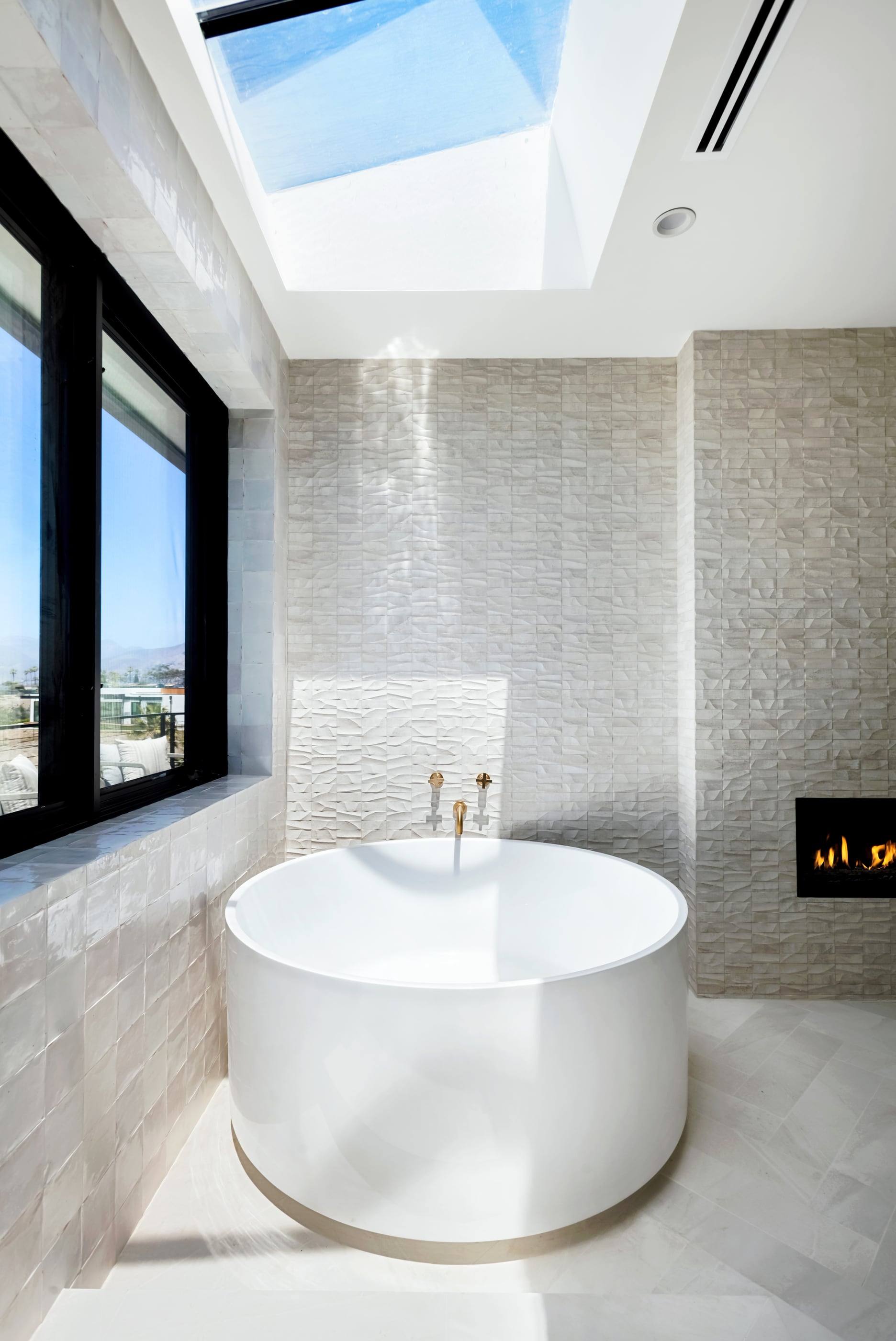 Round soaking tub beneath a skylight beside a fireplace