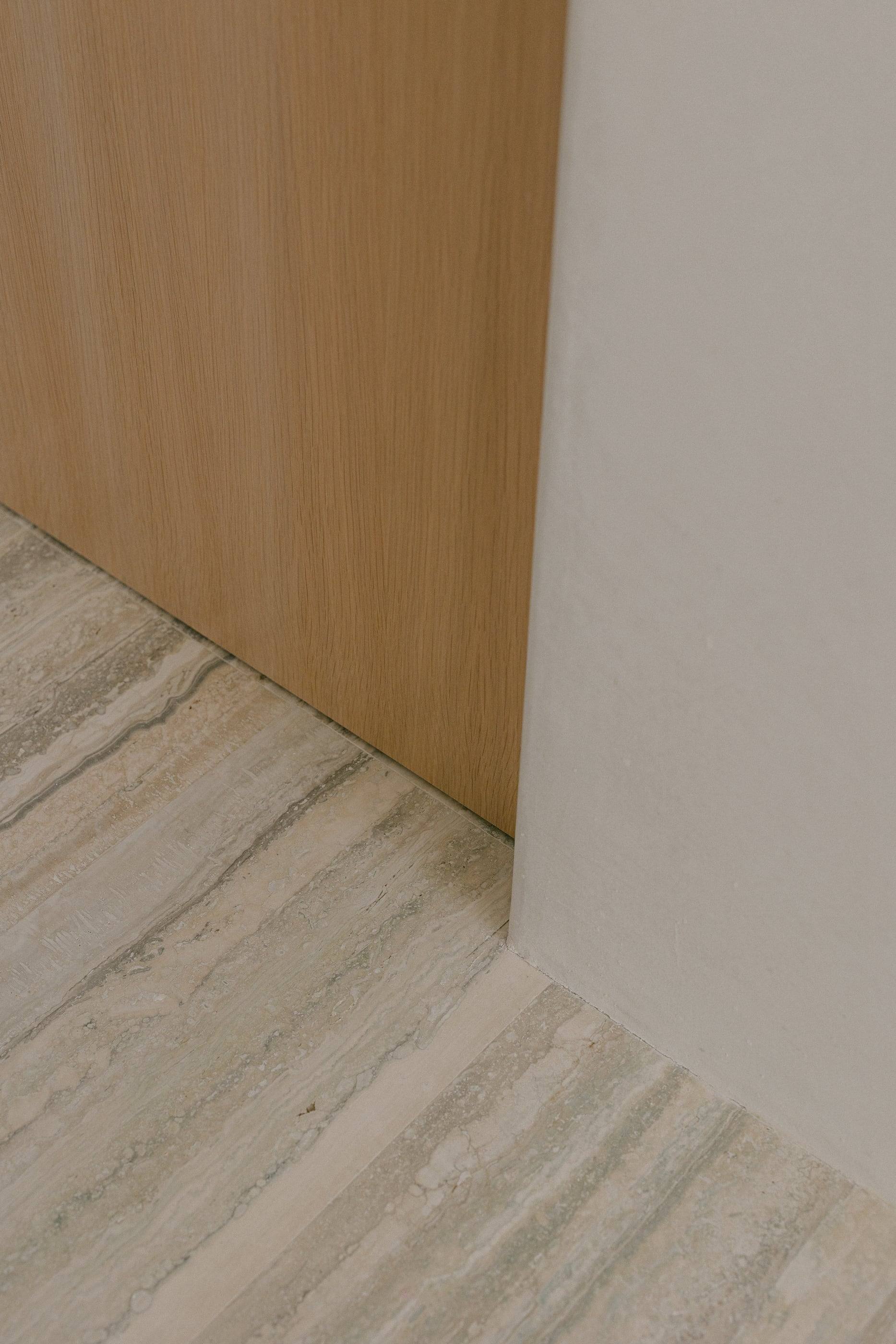 Detail where a travertine floor meets white oak and plaster