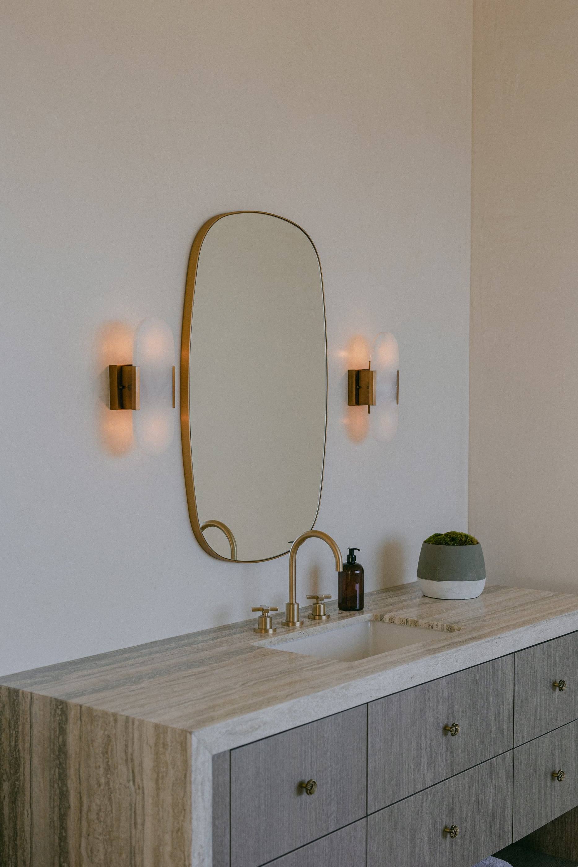 Travertine vanity with a brass-framed mirror and sconces